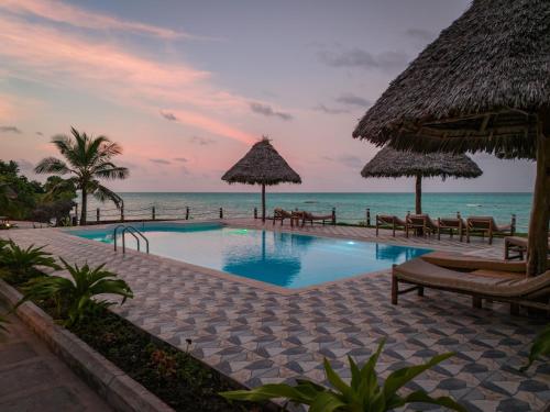 a pool at the beach with chairs and umbrellas at Mahi Mahi Beach Hotel in Jambiani