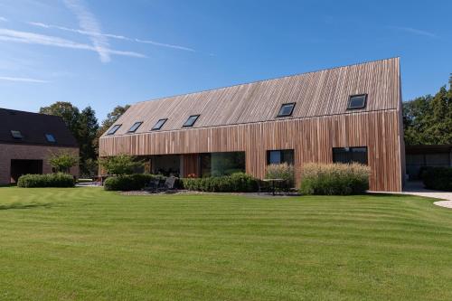 un edificio de madera con un gran patio de césped en Logies De Hoeven, en Kasterlee