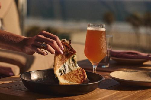 a person is holding a sandwich in a bowl next to a glass of beer at Hotel Erwin Venice Beach in Los Angeles