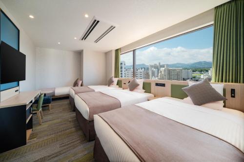 a hotel room with three beds and a large window at HOTEL MYSTAYS Miyazaki in Miyazaki