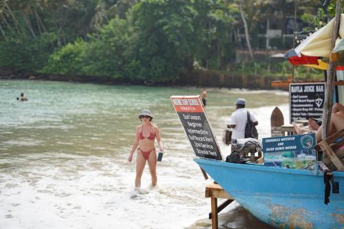 a woman in a bikini standing on a beach next to a boat at Hiricurry Hostel & Restaurant in Dickwella