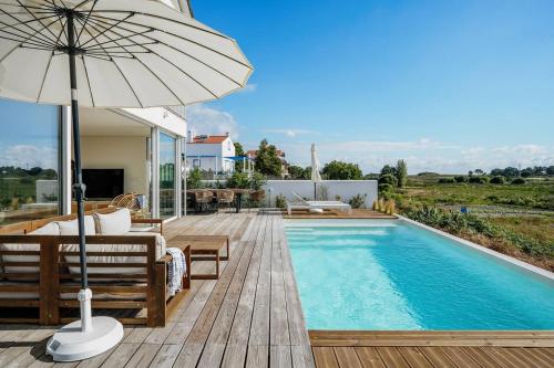 a swimming pool with an umbrella and chairs and a patio at Villa Possanco, Comporta beach villa in Comporta