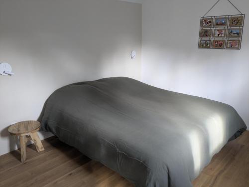 Una cama con una manta gris y un taburete de madera. en Au nid de cigo, en Sigolsheim