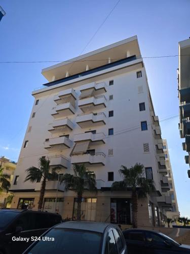 a tall white building with palm trees in front of it at Nova Apartaments Qerret in Golem