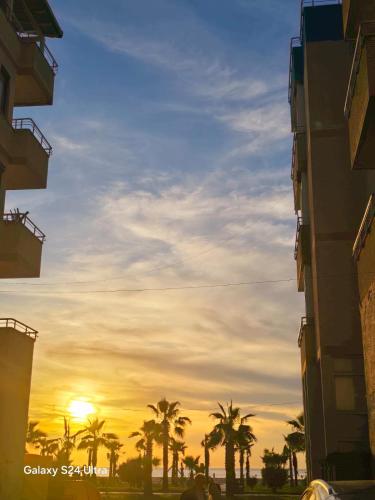 a sunset between two buildings and palm trees at Nova Apartaments Qerret in Golem