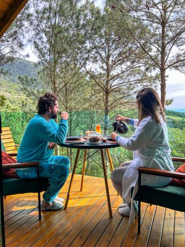 a man and woman sitting at a table on a deck at Chalés do Tabuleiro in Palhoça