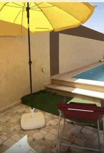 a yellow umbrella sitting next to a swimming pool at Maison piscine privée in Bū Shammah