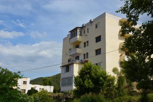 a tall white building with trees in front of it at Apartament Cela in Çorovodë