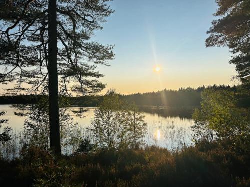 a view of a lake with the sun setting at Family-friendly red cottage in Småland in Lidhult
