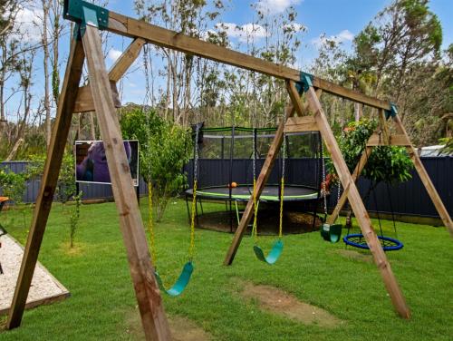 a wooden swing set in a yard with a man at Skyes Beach House-Views, Spas, Sauna, Arcade Games in Surf Beach
