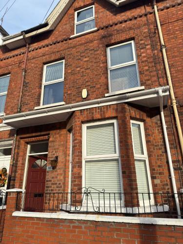 a red brick house with a balcony and a red door at Cozy House Great Location in Belfast