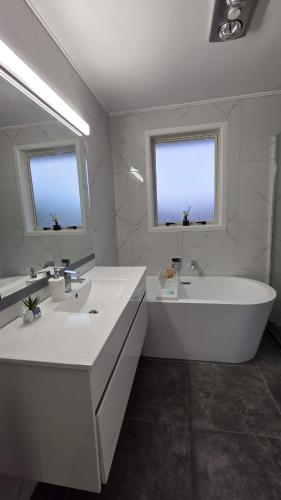 a bathroom with two sinks and a tub and two windows at Northshore Central Cosy & Comfortable 3BR Home in Auckland