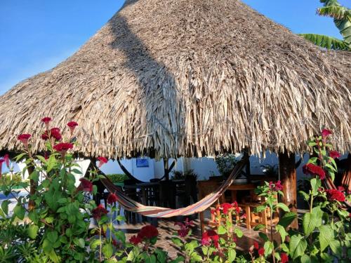 a straw hut with a hammock and red flowers at Cabaña Villa Carmen in Juan de Acosta