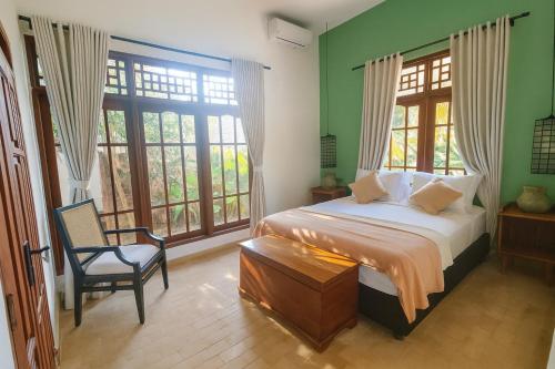 a bedroom with a bed and a chair and windows at Villa Andia in Gili Air