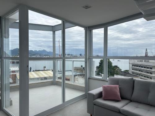 a living room with a couch and large windows at Studio moderno e novo - Uni Home 405 - Boa Viagem in Niterói