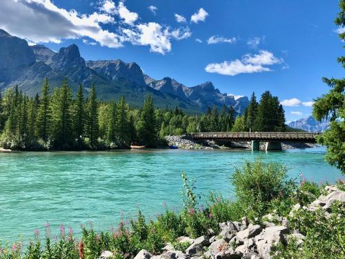 a bridge over a river with mountains in the background at Cascade Penthouse by Canadian Rockies Vacation Rentals in Canmore
