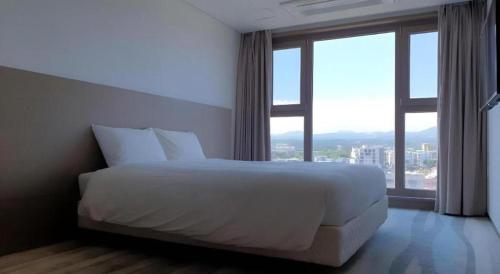 a white bed in a room with a large window at Ebenezer Hotel in Jeju
