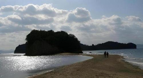 two people walking on a beach near the water at Country Inn The White Marine in Tonosho