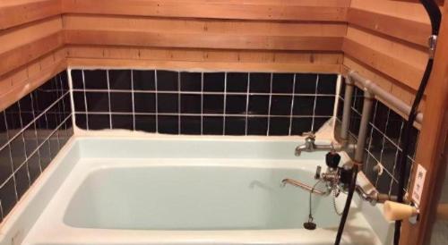a bath tub in a bathroom with black tiles at Kakeyu Onsen Hotel Kameya in Ueda