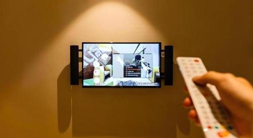 a person holding a remote control in front of a tv at IU Hotel Kunming Jinma Bijifang Joy City in Kunming