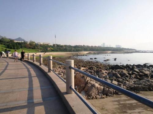 people walking on a sidewalk next to the beach at 7 Days Premium Qingdao World of Ocean Qingdao University in Qingdao