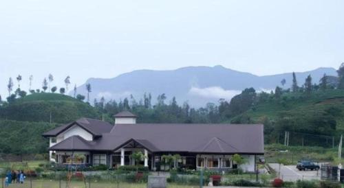 a large house in a field with mountains in the background at Talawakele Rest House in Nuwara Eliya