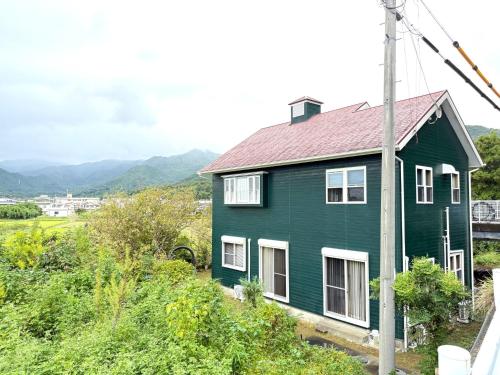 a green house with a red roof on a hill at 苔ハウスMoss House in Shingū