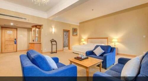 a living room with blue couches and a bed at Zhuhai Dehan Hotel in Zhuhai