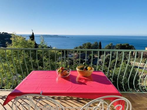 a red table with two bowls of fruit on a balcony at Gîte "Villa SIMONE" Vue Mer 180° CALME Terrasse couverte Jardin. in Carqueiranne