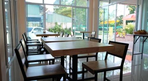 a restaurant with wooden tables and chairs and windows at Bees Smile Hotel in Chiang Rai