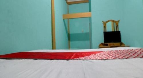 a bed with a red and white blanket and a chair at Hotel O Rania Kost Simpang Rimbo in Jambi