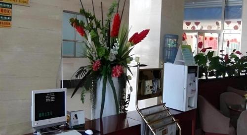 a vase of flowers sitting on a desk with a computer at GreenTree Inn Tianjin Wuqing Distric Bohai Market in Tianjin