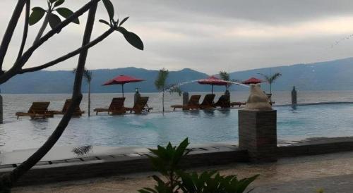 a swimming pool with chairs and umbrellas in the water at Samosir Cottages Resort in Tuk Tuk
