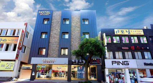 a tall blue building with shops in a city at Jeju Sejong Hotel in Jeju