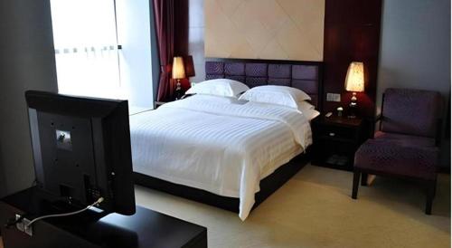 a bedroom with a bed with white sheets and a tv at Oriental Hotel in Dongguan