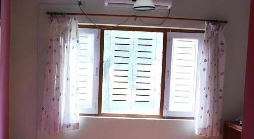 a window with white shutters and pink curtains in a room at New Dakshinkali Village Resort in Kathmandu