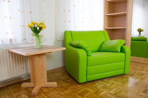 a green chair and a table with a vase of flowers at Hotel Restaurant Thadeushof in Techelsberg am Worthersee