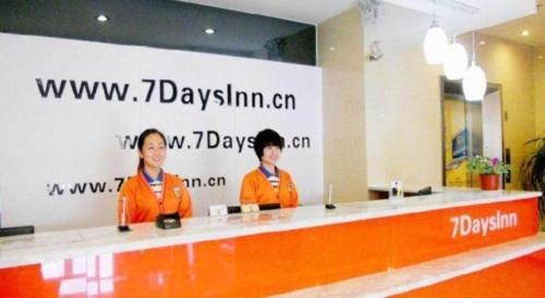 two women in orange jackets standing behind a counter at 7 Days Inn Weihai High-Speed Railway & Bus Station in Weihai