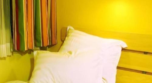 a bed with a white pillow against a yellow wall at 7 Days Inn Hohhot Hailiang Xinhua Square Metro Station in Hohhot