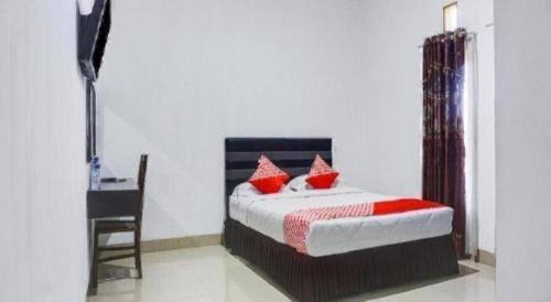 a bedroom with a bed with red pillows and a desk at Capital O 91534 Wisma Metro Permai in Makassar