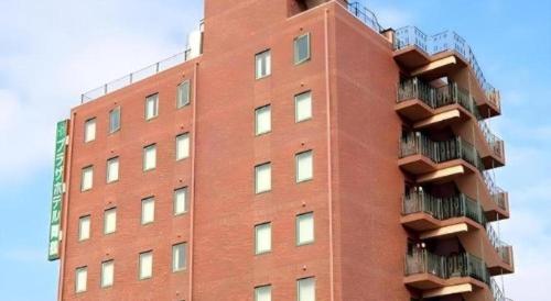 a tall red brick building with balconies on it at APA Hotel Nishimaizuruekimae in Maizuru