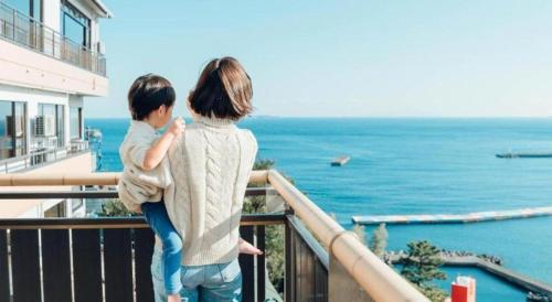 a woman and child standing on a balcony looking at the ocean at Tsukino Sumika Atami Juraku Hotel in Atami