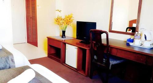 a desk with a television and a vase of flowers on it at Global Hotel Labuan in Labuan