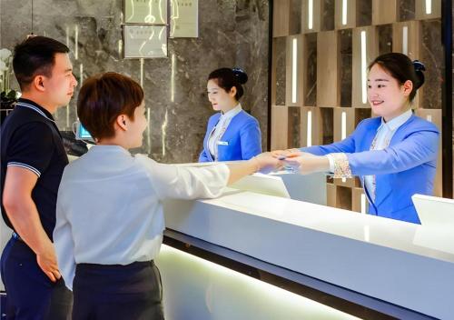 a man shaking the hand of a woman at a counter at Echarm Hotel Guizhou Xingyi Jushan Avenue in Xiawutun