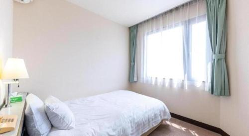 a white bedroom with a bed and a window at Tabist Hotel New Osamura Sabae in Fukui