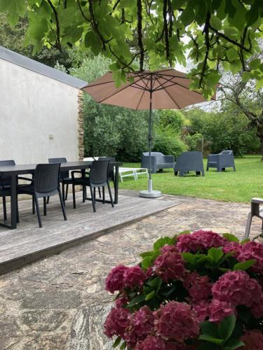 a table and chairs with an umbrella and flowers at Gîte de Charme en bord de Loire in Le Pellerin