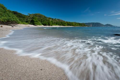 a beach with a wave washing up on the sand at Tambor Tropical Beach Resort- Adults Only in Tambor