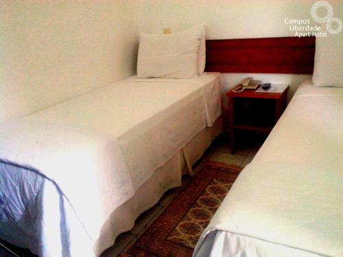 two beds in a small room with a night stand at Campus Liberdade Flat in Belo Horizonte