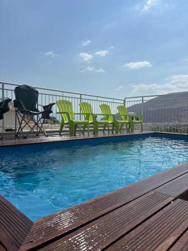 a swimming pool with green chairs on a balcony at תכלת במושבה Lite Blue in the colony in Migdal