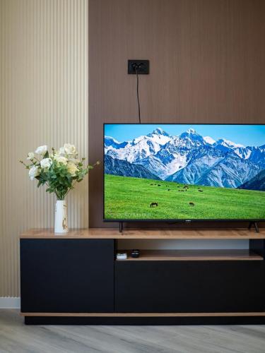 a flat screen tv on a stand with a vase of flowers at Комфортная евродвушка у проспекта Абая, рядом с метро in Almaty